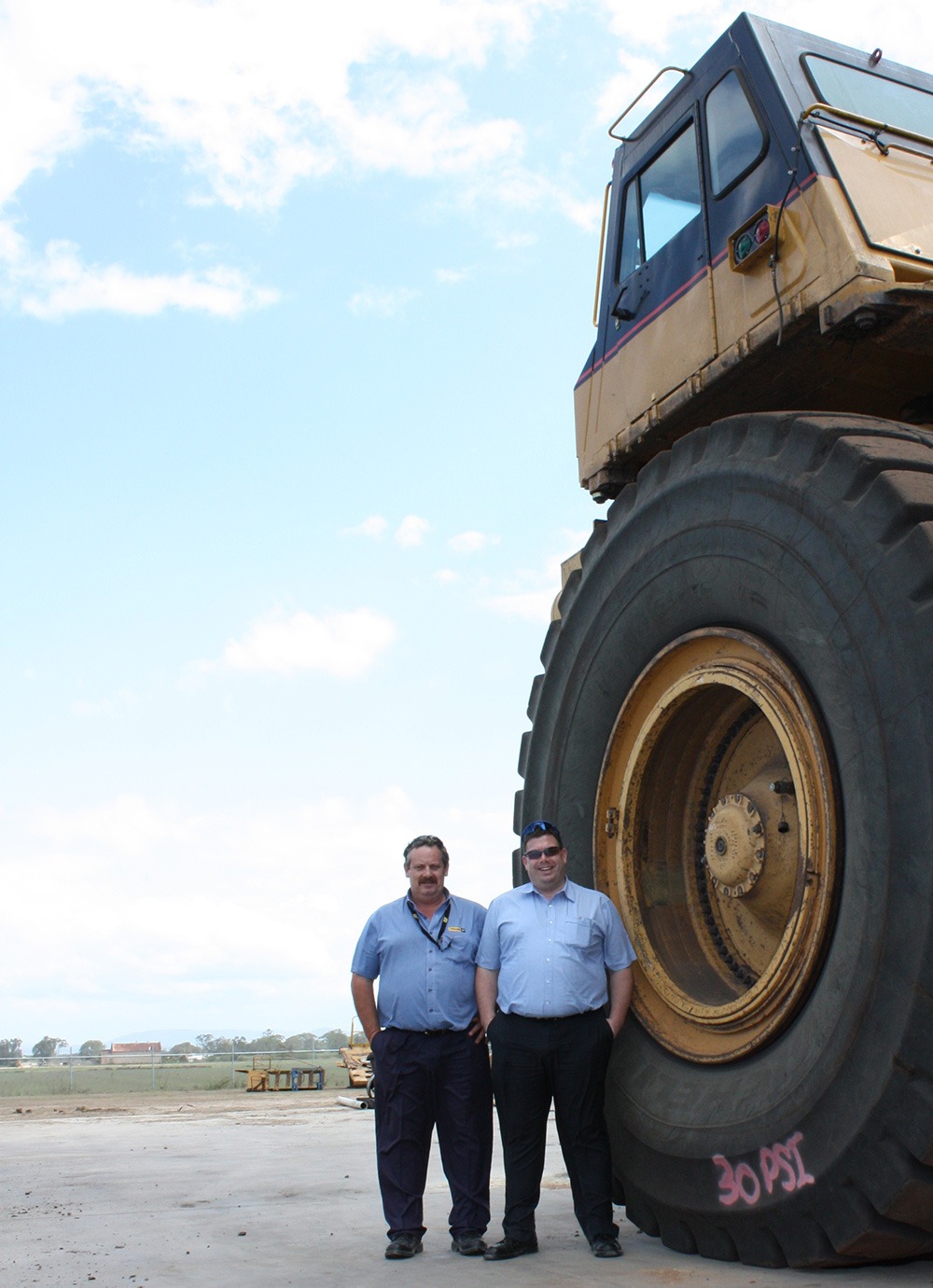 Dennis Hickman and Craig Freeman of Hastings Deering standing beside the wheel of a Caterpillar mining loader, photographed in 2011
